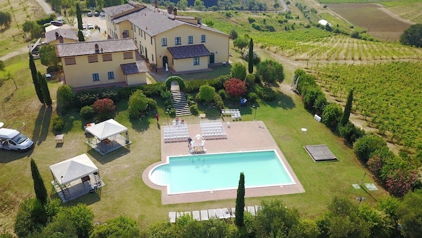 A large house with a swimming pool, surrounded by a vineyard and a well-maintained lawn.