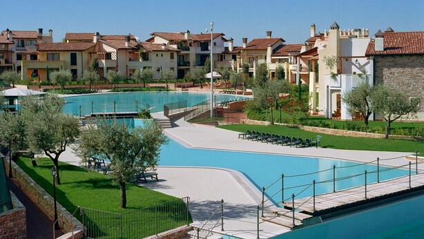 A resort with multiple swimming pools, a well-maintained lawn, and a row of Mediterranean-style villas.