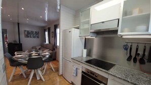 Une cuisine compacte équipée d’un four encastré, d’une plaque de cuisson et d’un réfrigérateur. On y trouve un coin repas avec une table et des chaises, ainsi qu’un canapé à l’arrière-plan.