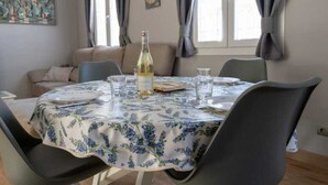 Un coin repas avec une table ronde, des chaises, une bouteille de vin et une horloge au mur.