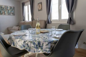 A dining area with a round table, chairs, a bottle of wine, and a clock on the wall.