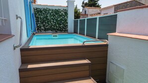 Une piscine avec des marches menant à son bord, entourée d’un mur blanc et d’un mur vert orné d’un motif végétal.
