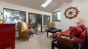 A living room with a red sofa, two armchairs, a wooden coffee table, and a ship's wheel decoration.