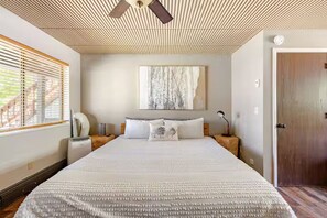A bedroom with a large bed, a ceiling fan, a painting on the wall, and a wooden door.