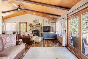 A cozy living room with a fireplace, wooden beams, a television, and a large window.