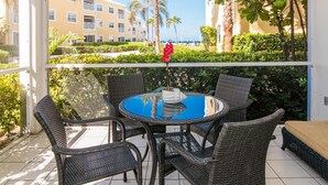 A round table with wicker chairs on a balcony with a view of a hotel building and palm trees. - Regal Beach Club #513 (Seven Mile Beach)