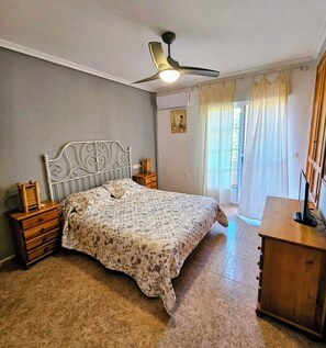 A bedroom with a bed, a nightstand, a dresser, a ceiling fan, and a window with curtains. - Townhouse in front of Botanical Garden, Salinas and Natural Park (Lo Pagan)