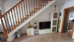 A staircase with wooden balusters, a flat-screen TV on a white entertainment unit, a refrigerator, and a tiled floor. - Townhouse in front of Botanical Garden, Salinas and Natural Park (Lo Pagan)