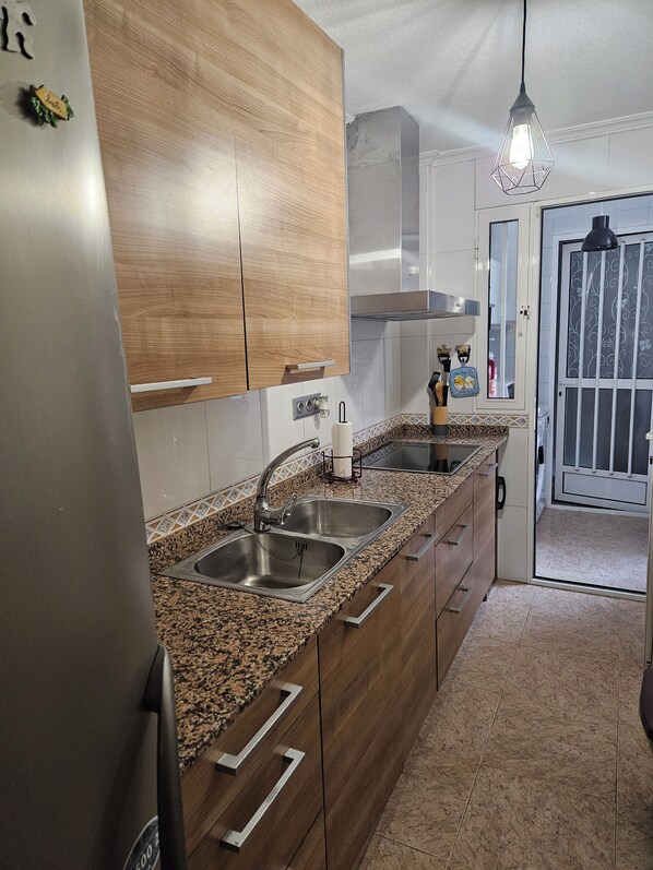 A kitchen with granite countertops, stainless steel appliances, wooden cabinets, and a hanging light fixture.
