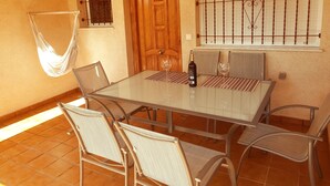 A dining area with a glass table, wicker chairs, a wooden door, a barred window, and a hanging hammock. - Townhouse in front of Botanical Garden, Salinas and Natural Park (Lo Pagan)