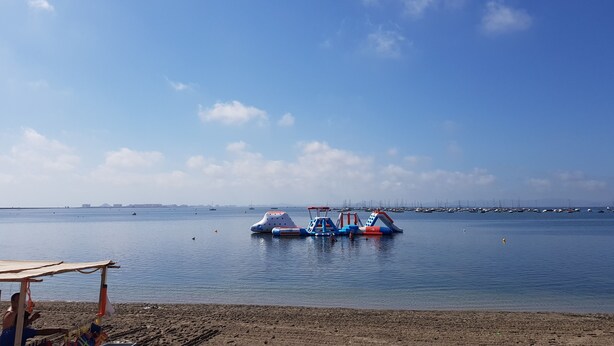 A beach with a sandy shore and a calm sea. There are inflatable water toys in the water and a few boats in the distance. - Townhouse in front of Botanical Garden, Salinas and Natural Park (Lo Pagan)