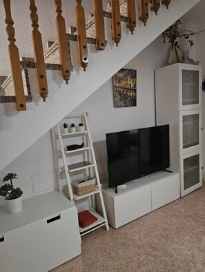 A living room with a television on a white cabinet, a white ladder, and a painting on the wall. - Townhouse in front of Botanical Garden, Salinas and Natural Park (Lo Pagan)