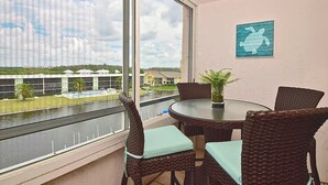 Ein Balkon mit Korbmöbeln, Blick auf ein Gewässer und ein Gebäude im Hintergrund.