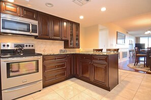 A kitchen with built-in appliances, wooden cabinets, and a dining area with chairs.