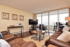 A living room with a sofa set, a coffee table, a TV, and a balcony with outdoor furniture.