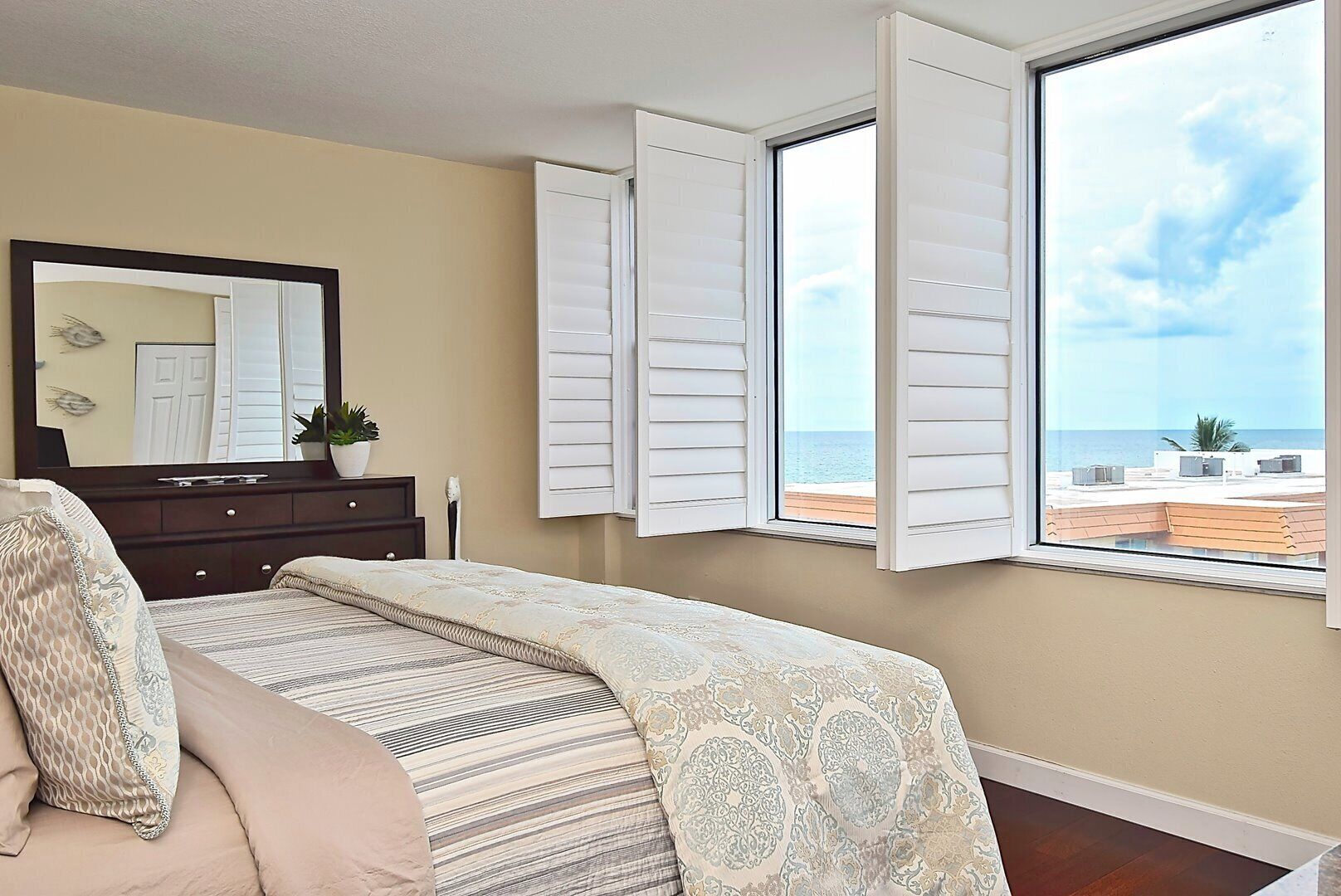 A bedroom with a bed, a dresser, a mirror, and a window with shutters.