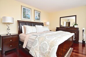 Een slaapkamer met een groot bed, twee nachtkastjes, een dressoir, een spiegel en twee ingelijste foto's aan de muur.
