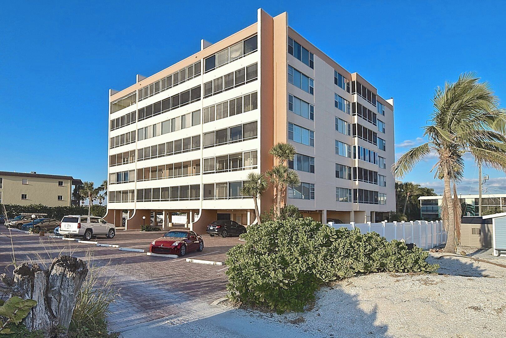 A multi-story hotel with a parking lot, palm trees, and a clear blue sky.