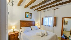 A bedroom with a wooden headboard, a bed with white linens, two bedside lamps, a mirror, and a window with curtains.