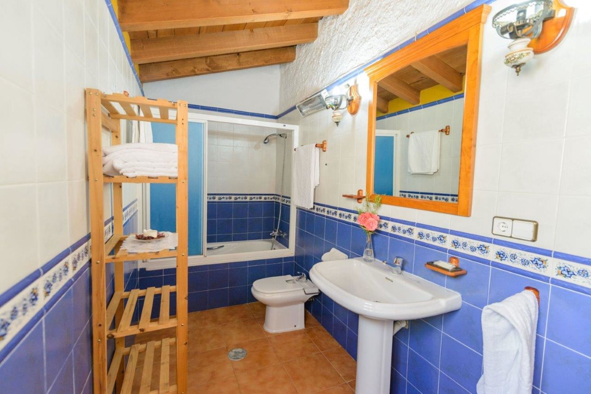 Un baño con estante de madera, bañera, inodoro y lavabo.