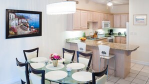 Une cuisine moderne dotée de plans de travail en granit, d’un îlot central et d’un coin repas avec des tables et des chaises rondes en verre.
