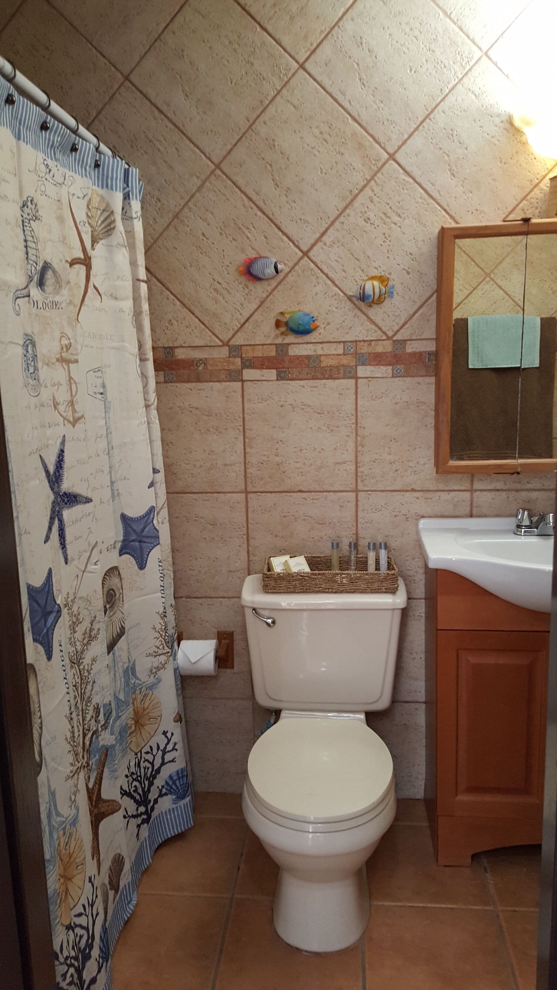 Een badkamer met toilet, wastafel en een douchegordijn met afbeeldingen van zeedieren, en een betegelde muur met decoratieve vissen.