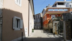 Uma rua estreita com edifícios de ambos os lados, incluindo um edifício bege com persianas e um edifício vermelho com varanda.