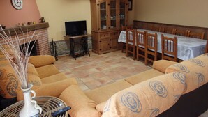 Een woonkamer met een zithoek, een televisie, een kast en een eettafel met stoelen.