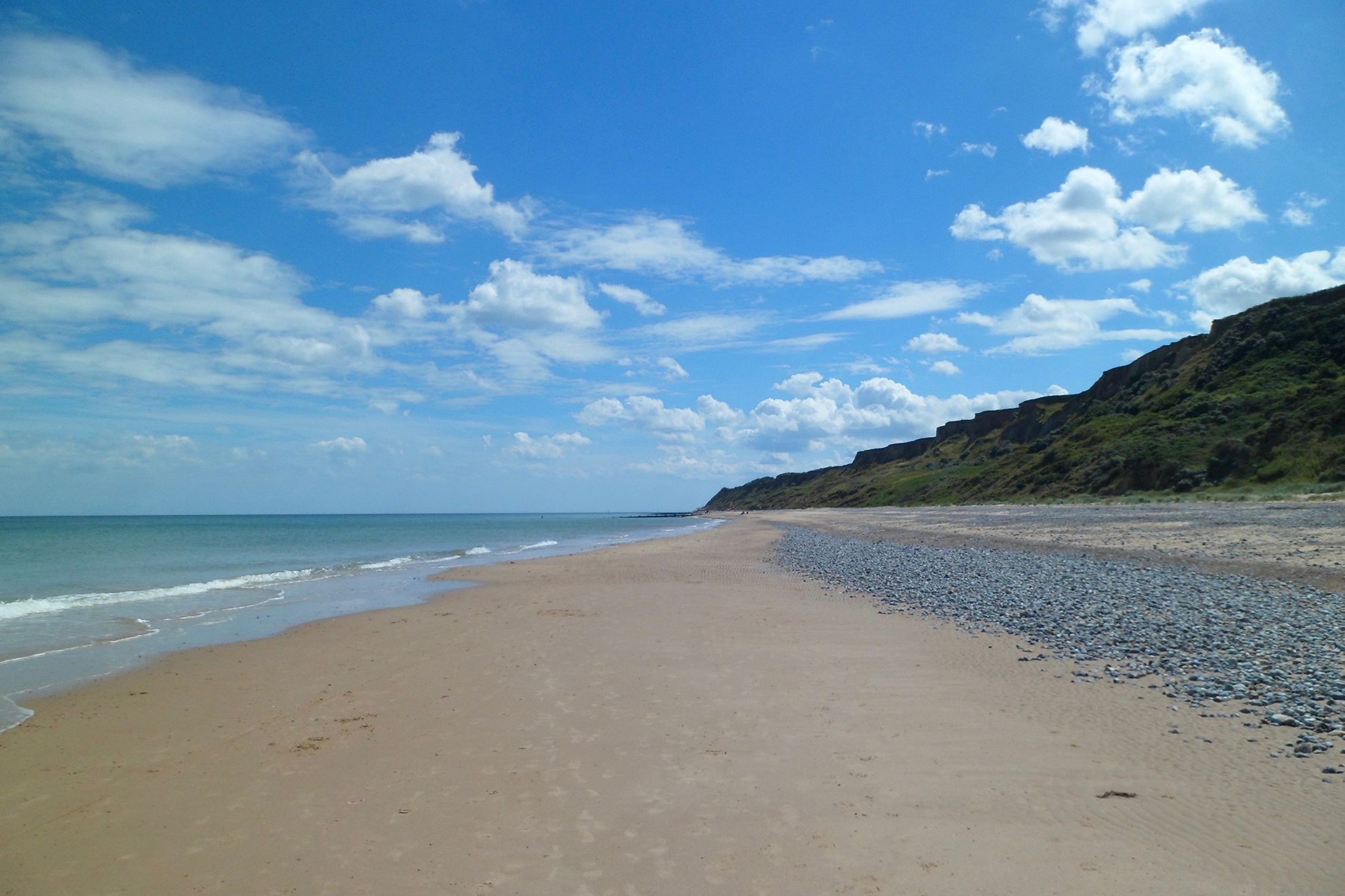 A beach with a pebbly shore, calm sea, and a hilly landscape in the background.