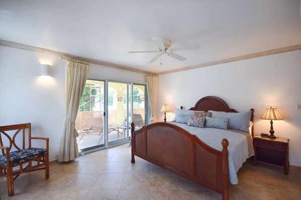 A bedroom with a bed, two bedside tables with lamps, a chair, a ceiling fan, and a sliding glass door leading to an outdoor area.