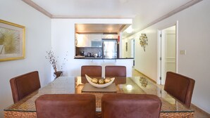 Un comedor con mesa de vidrio y sillas marrones, que conduce a una cocina con electrodomésticos modernos.