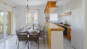 A modern kitchen with white cabinets, a wooden island, and a dining area with a table set for four. - 0304 Monte Verde Naranja (Javea / Xàbia)