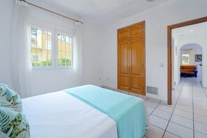 A bedroom with a bed, a wooden wardrobe, a window with curtains, and a view of an outdoor area. - 0304 Monte Verde Naranja (Javea / Xàbia)