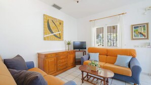 A living room with a sofa, a wooden cabinet, a television, and a painting on the wall. - 0304 Monte Verde Naranja (Javea / Xàbia)