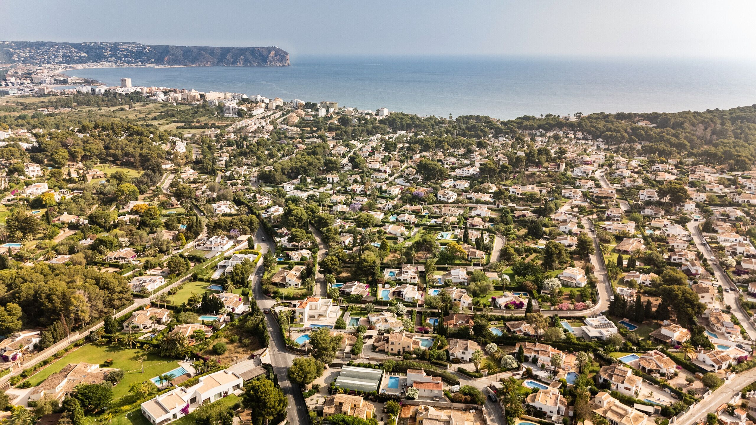 An aerial view of a coastal residential area with houses, roads, and a coastline.
