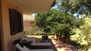 A sunlit patio with two lounge chairs, a table, and potted plants.