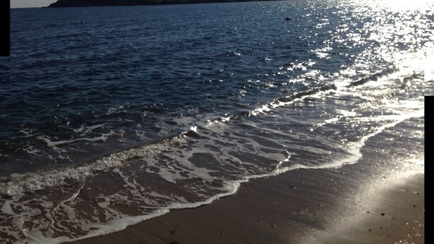 A beach with waves gently lapping onto the shore, a clear sky, and a distant landmass.