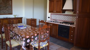 A dining area with a table covered in a floral tablecloth, surrounded by wooden chairs.