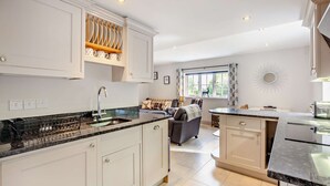 A modern kitchen with white cabinetry, a granite countertop, and a built-in dishwasher. There is a dining area with a sofa and a table, and a large window providing natural light.