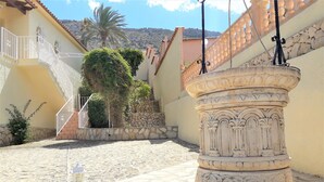 Ein Innenhof mit einem Steinfbrunnen, einer Treppe und einer Palme.