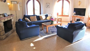 Ein Wohnzimmer mit einem blauen Sofa, zwei Sesseln, einem Couchtisch, einem Fernseher und einem Kamin.