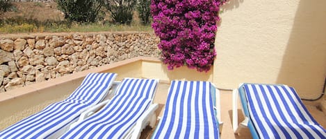 A poolside area with four striped lounge chairs and a stone wall.