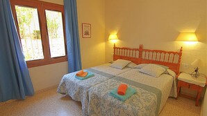 Ein Doppelzimmer mit zwei Betten, jeweils mit einer blau-weißen Musterdecke, und einem Holzkopfstück. Es gibt zwei Nachttischlampen und einen kleinen Tisch mit einer Lampe darauf.