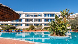 Ett hotell med en swimmingpool, blå stolar och ett parasoll med halmtak.