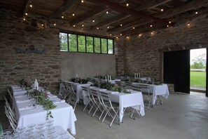 A stone-walled room with tables set for a formal event, featuring string lights and a large window.