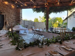 An outdoor dining area with a stone wall, a covered barbecue, and a table set for a meal.