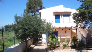 Une maison à deux étages, dotée d’une façade blanche et de touches de bleu, entourée de verdure et d’arbres.