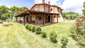 A stone house with a covered patio, a barbecue area, and a garden with a lawn and shrubs. - Hilltop farmhouse with pool and sea view (pereta (GR))