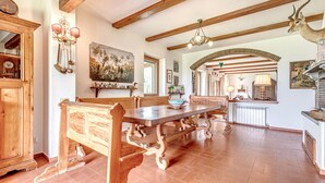 A spacious dining area with a wooden table and benches, a kitchen with a stone column, and a rustic ceiling with exposed beams. - Hilltop farmhouse with pool and sea view (pereta (GR))