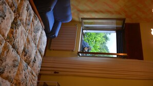 Una stanza con un letto, una finestra con persiane e vista sul verde.